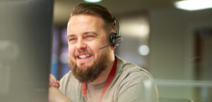 A bearded man wearing a headset at Reliance Technology Cares in-house Monitoring Centre helping its users.