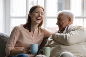 Grandparent and grand daughter smiling and laughing on the sofa with a mug in their hands