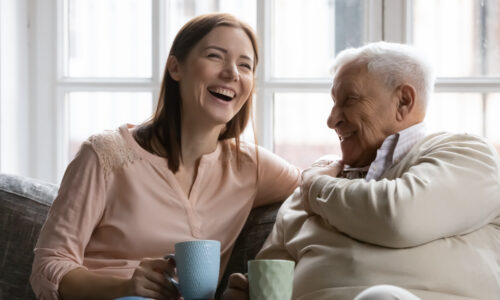 Grandparent and grand daughter smiling and laughing on the sofa with a mug in their hands