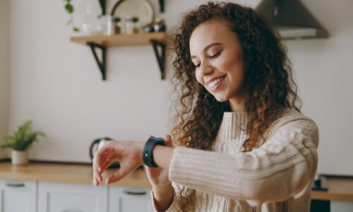 Young woman standing in her kitchen smiling while she looks at her smartwatch